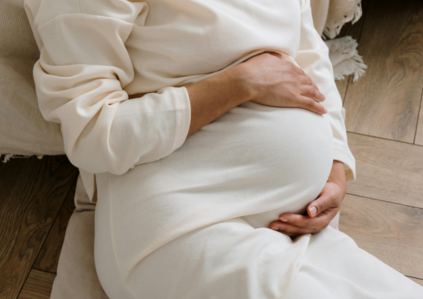 Frau liegt auf dem Boden und hält sich ihren schwangeren Bauch